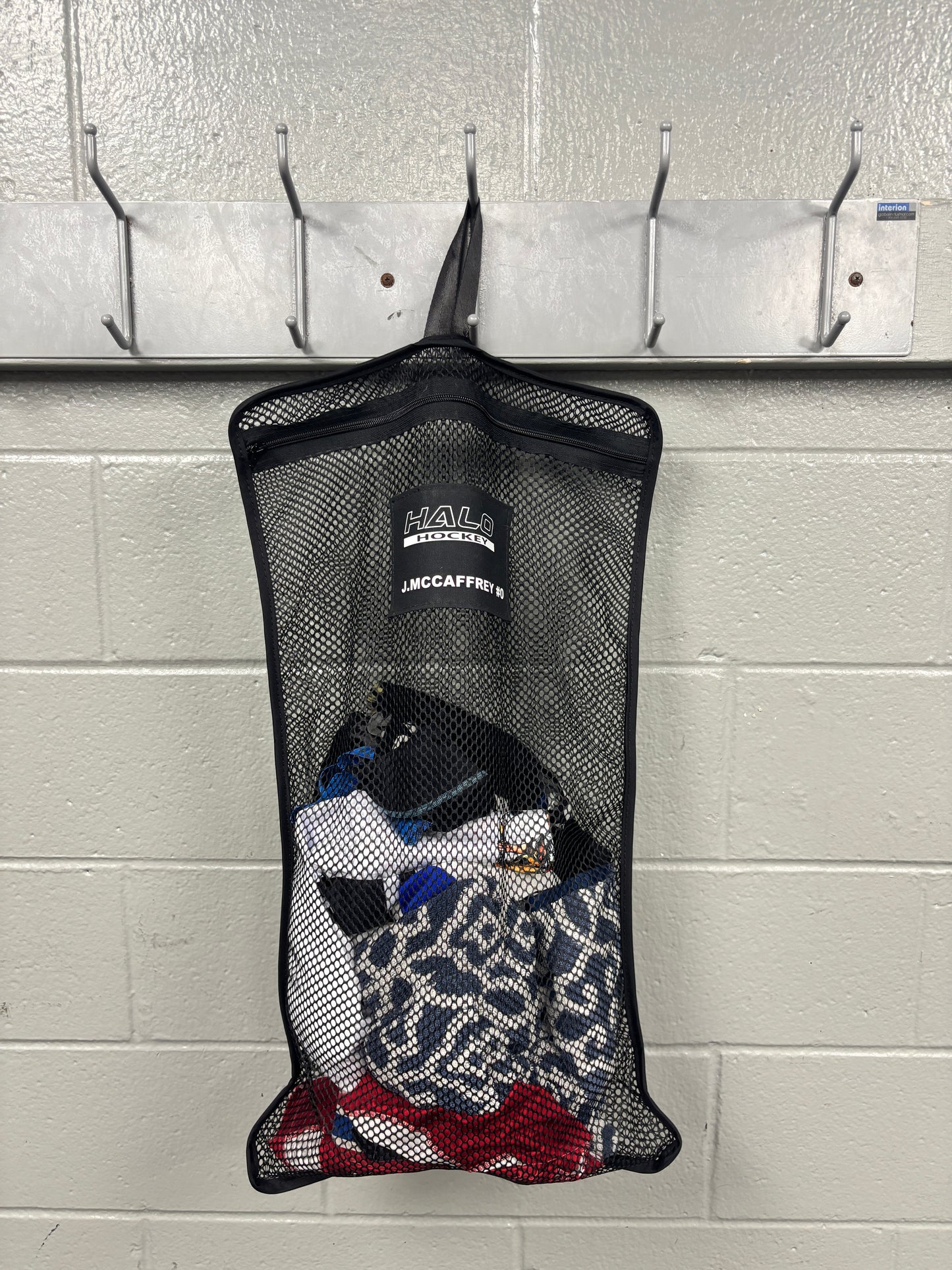 Full product view of Halo Hockey Stinky Boy laundry bag shown with custom name and number option half loaded with laundry hung in a locker room