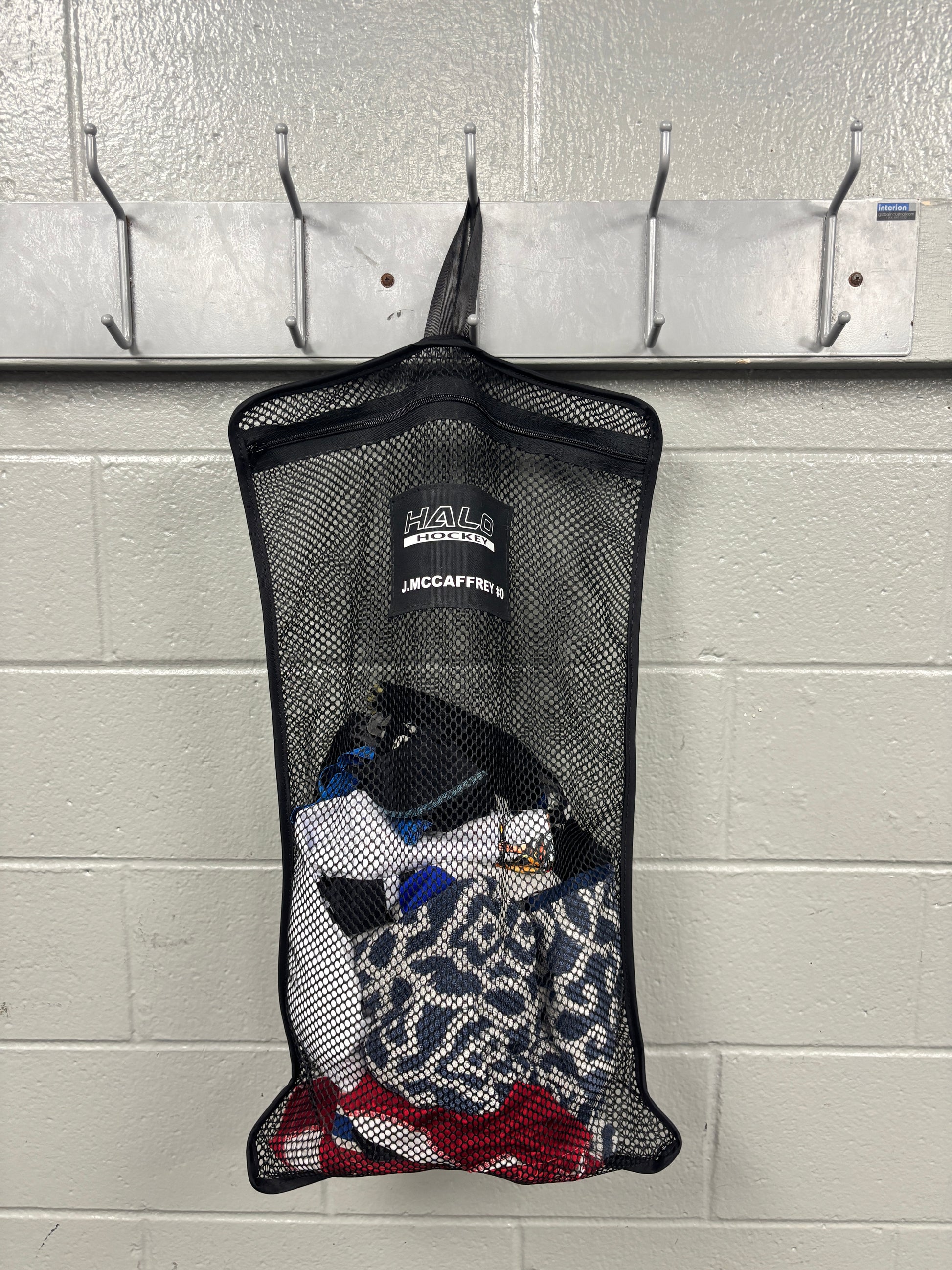 Full product view of Halo Hockey Stinky Boy laundry bag shown with custom name and number option half loaded with laundry hung in a locker room
