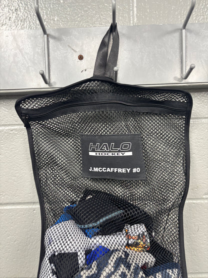 Closeup view of black Halo Hockey Stinky Boy laundry bag with custom name and number shown half full of hockey laundry hung on a locker room wall hook